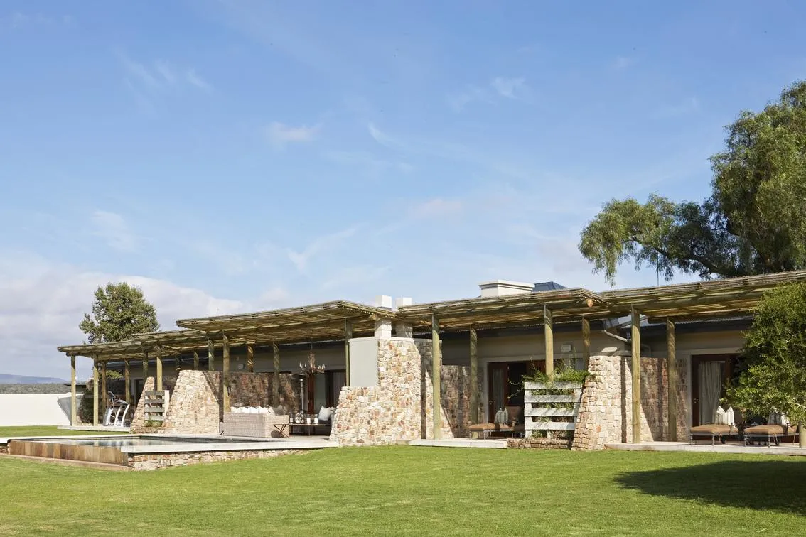 Fort House villa exterior — stone-and-pergola architecture with infinity pool and sweeping lawn