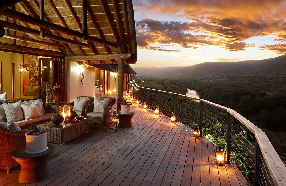 Covered lodge deck with cushioned chairs and lanterns at sunset overlooking the Great Fish River valley