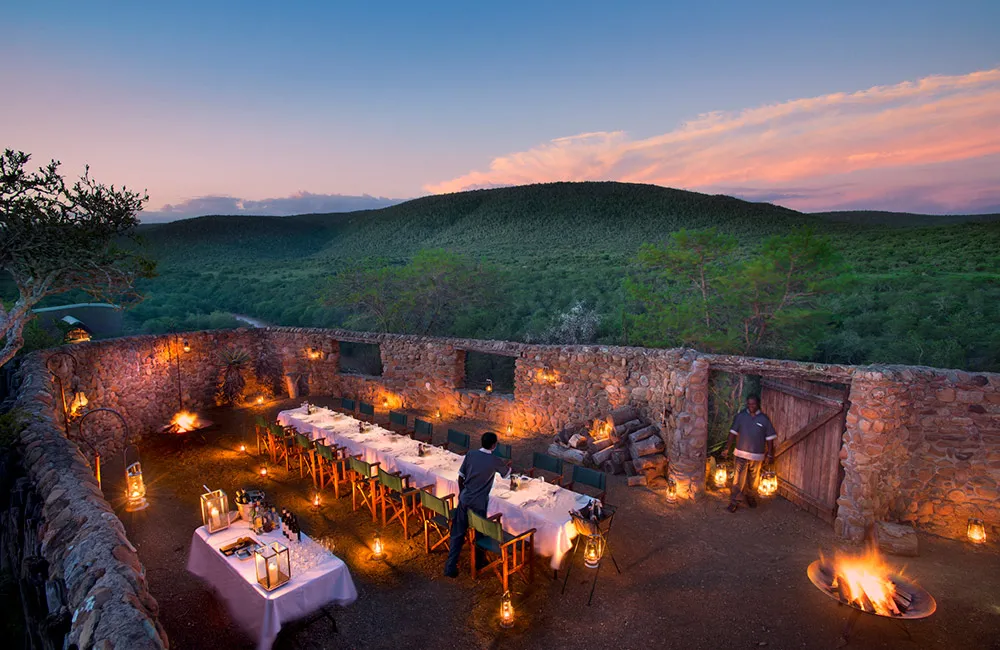 Stone-wall boma at twilight set with long candle-lit dining table