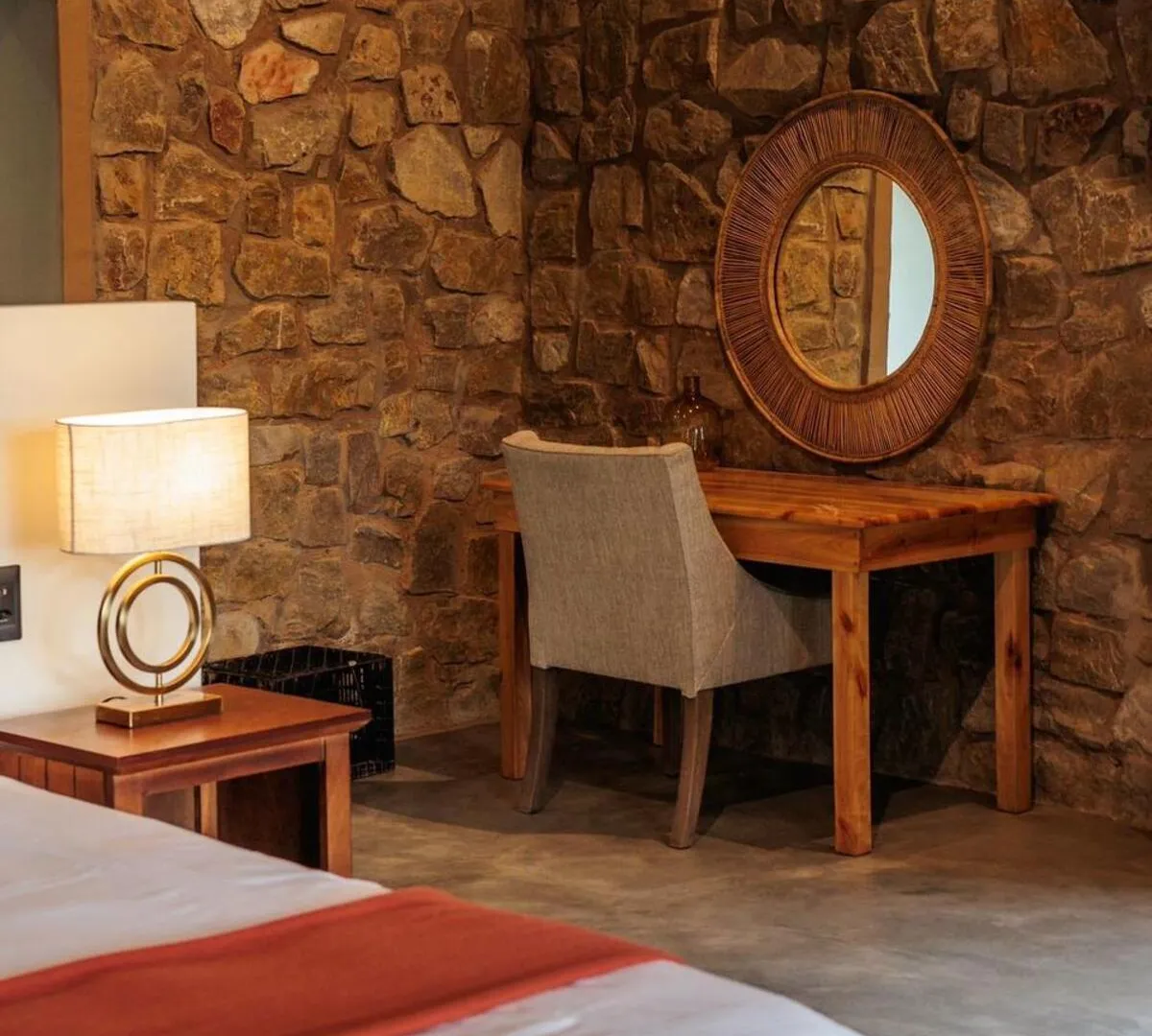 Suite bedroom corner with stone wall, writing desk and sunburst mirror