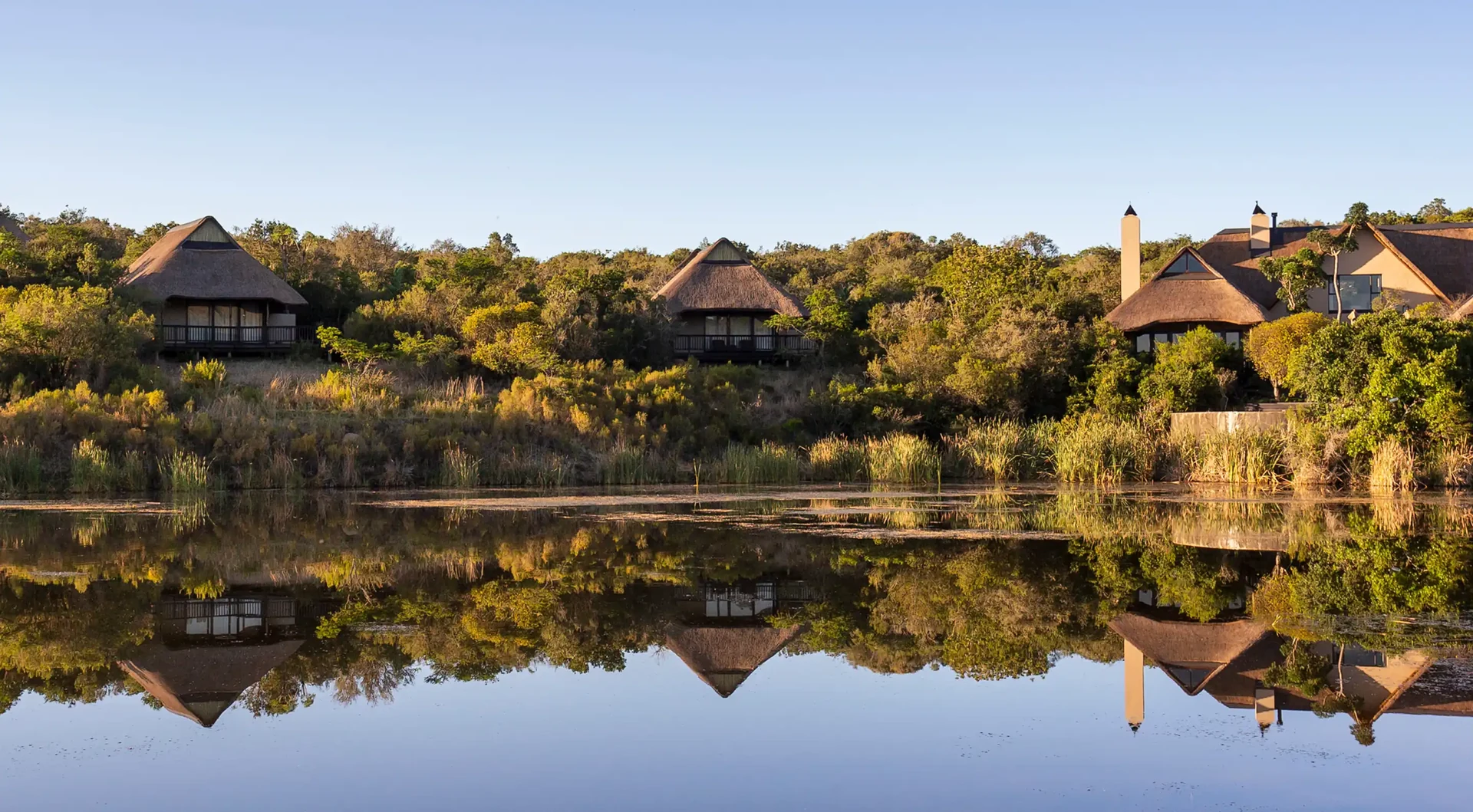 Kichaka thatched chalets reflected in the waterhole at sunrise