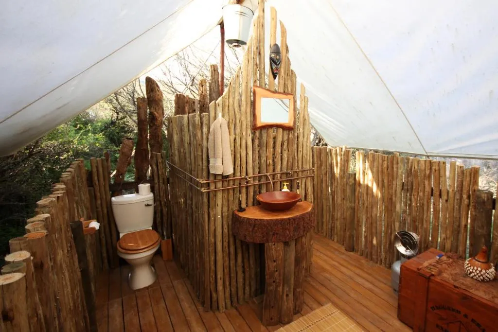 Tent bathroom interior with rustic timber-pole walls, wooden vanity and canvas roof