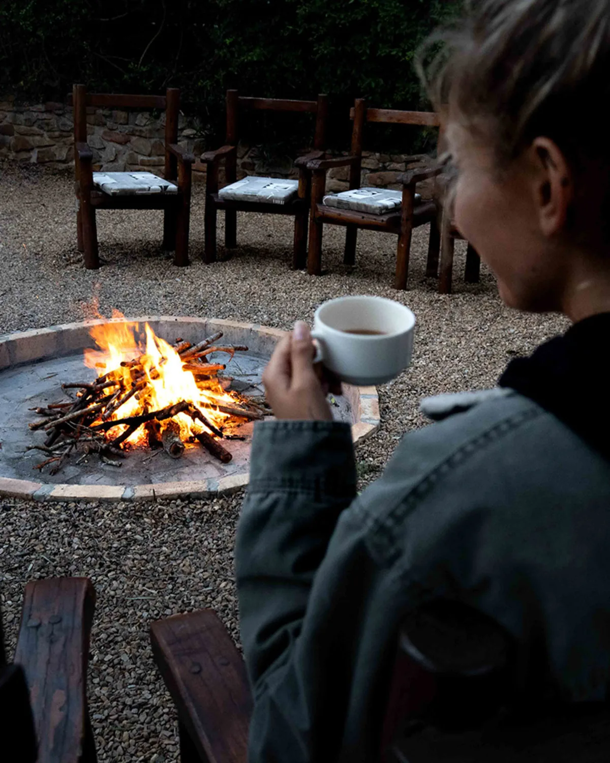 Fire pit at dusk — a guest with morning coffee by the boma